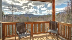 A wooden deck with two chairs and a view of mountains and trees.