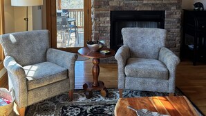 A living room with a stone fireplace, two patterned armchairs, a coffee table, and a rug.