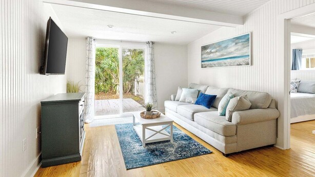 A modern living room with a sofa, coffee table, and a TV. - Charming Folly Beach Home - Perfect Location (Folly Beach)