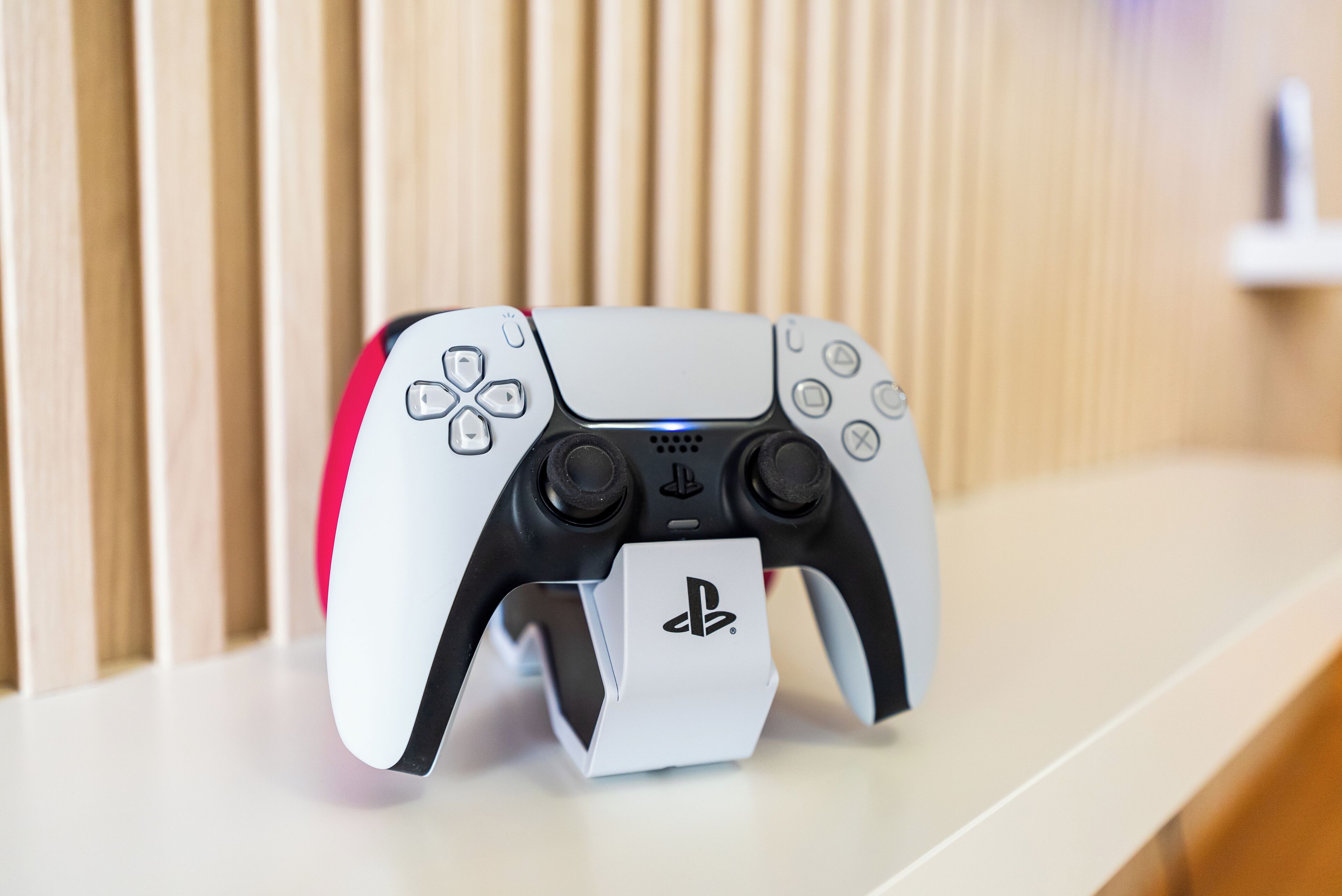 A PlayStation 5 controller on a white surface with a wooden background.