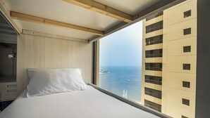 A hotel room with a large window, a bed, and a view of the sea. - YouSleep Hostel (Dubai)
