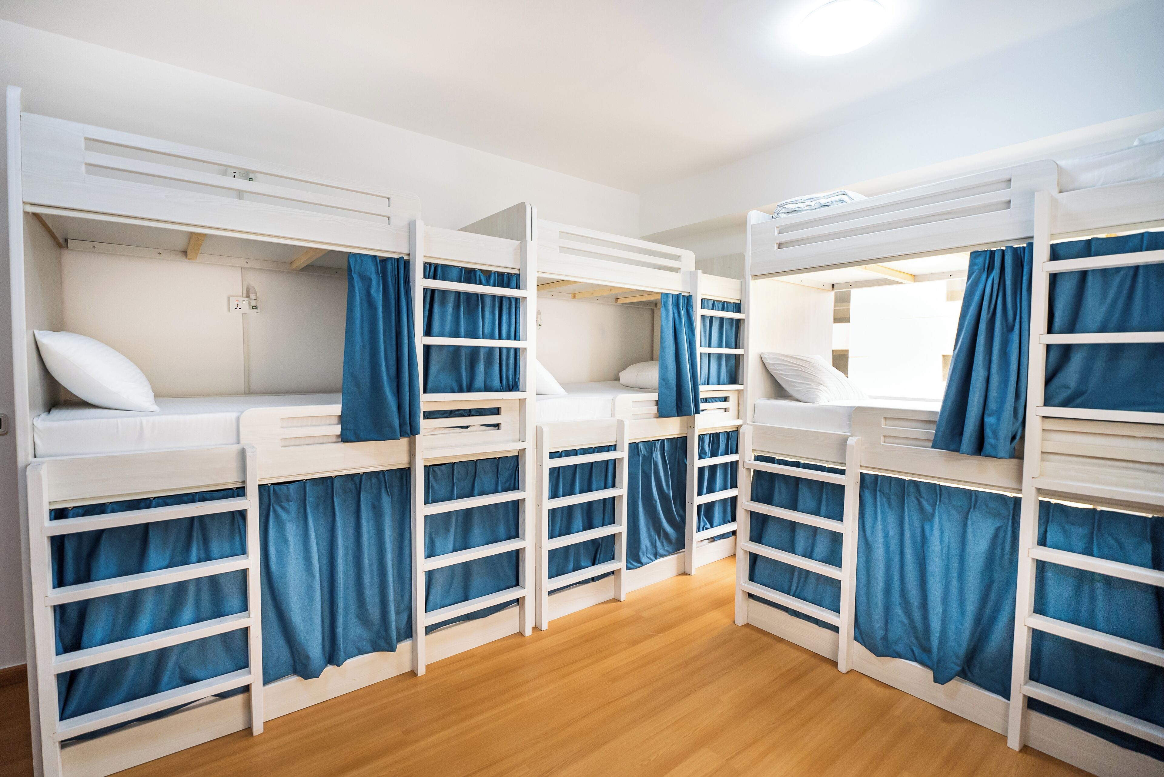 Een kamer met stapelbedden, houten vloeren en blauwe gordijnen.