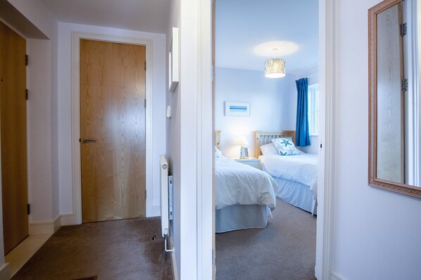 Ein Hotelzimmer mit Holztür, einem Bett mit weißer Bettwäsche, einem Nachttisch mit Lampe und einem großen Spiegel an der Wand.