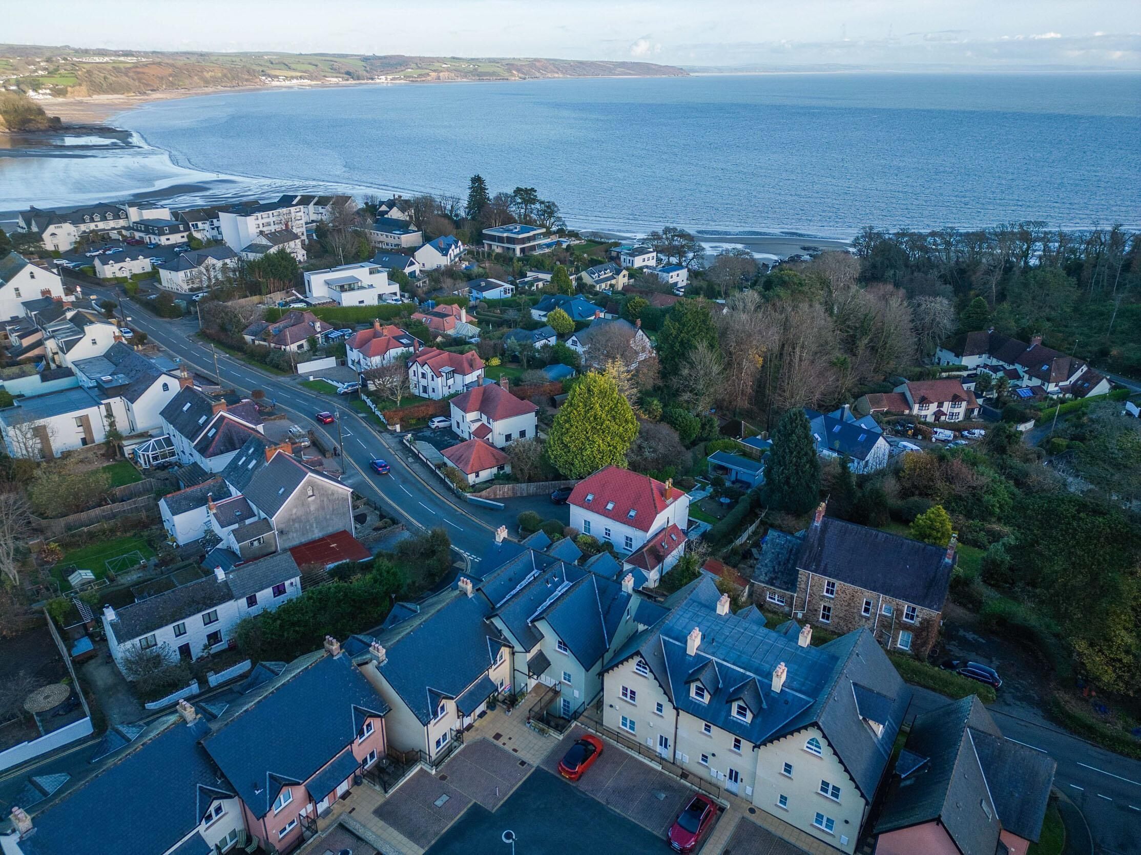 An aerial view of a coastal residential area with houses, roads, and a beach in the background.