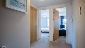 Een gang die leidt naar een slaapkamer met een bed, een bureau en een stoel.