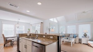 Eine moderne Küche mit Granit Arbeitsplatten, Edelstahlgeräten und einem Essbereich mit Korbstuhl und Tisch.