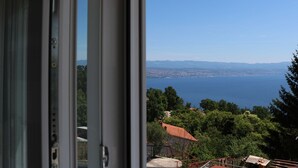 A view from a window overlooking a coastal landscape with a clear sky, distant mountains, and a body of water.
