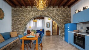 Une cuisine chaleureuse avec une arche en pierre, des armoires bleues et une table à manger en bois, accompagnée de chaises.