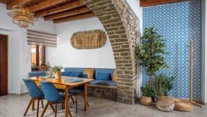 Un coin repas chaleureux avec une table en bois et des chaises bleues, un mur en pierre et un mur orné d’un motif bleu.