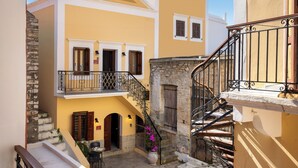 Une cour avec un bâtiment jaune, un escalier en pierre et un balcon orné d’une balustrade en fer forgé.