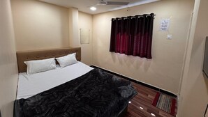 A hotel room with a bed, a ceiling fan, a window with curtains, and a small rug on the floor. - Hotel Shree Parwati Palace (Ujjain)