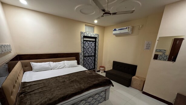 A bedroom with a bed, a sofa, a ceiling fan, an air conditioner, and a tiled floor. - Hotel Shree Parwati Palace (Ujjain)
