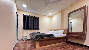 A bedroom with a wooden bed, a ceiling fan, a mirror, and a small bedside table. - Hotel Shree Parwati Palace (Ujjain)