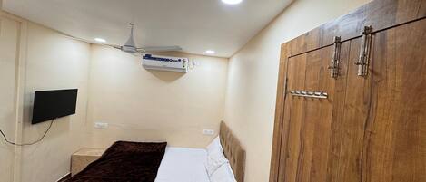 A bedroom with a bed, a wardrobe, a ceiling fan, an air conditioner, and a mounted TV.