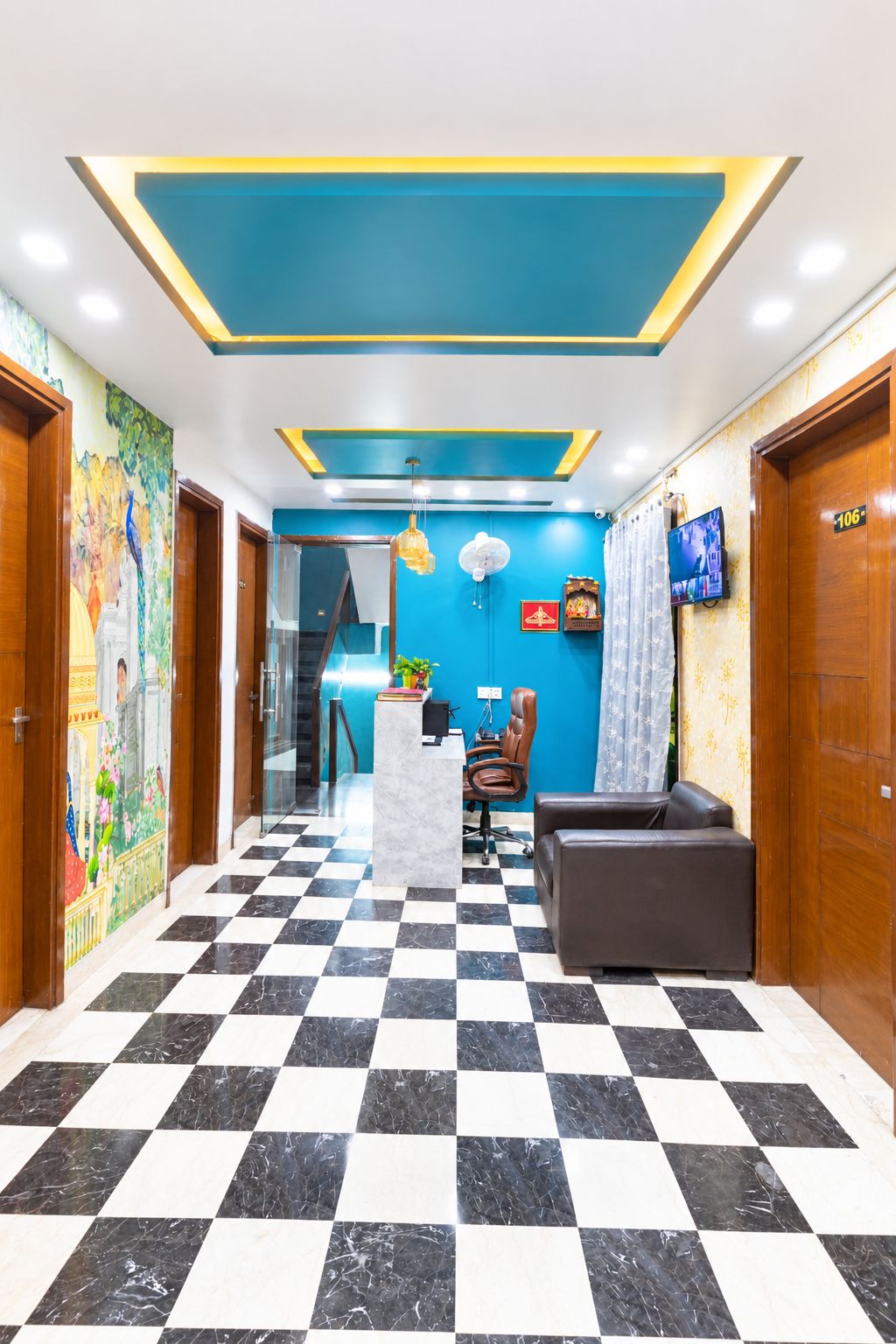 A hotel lobby with a checkered floor, a reception desk, a seating area, and a blue accent wall.