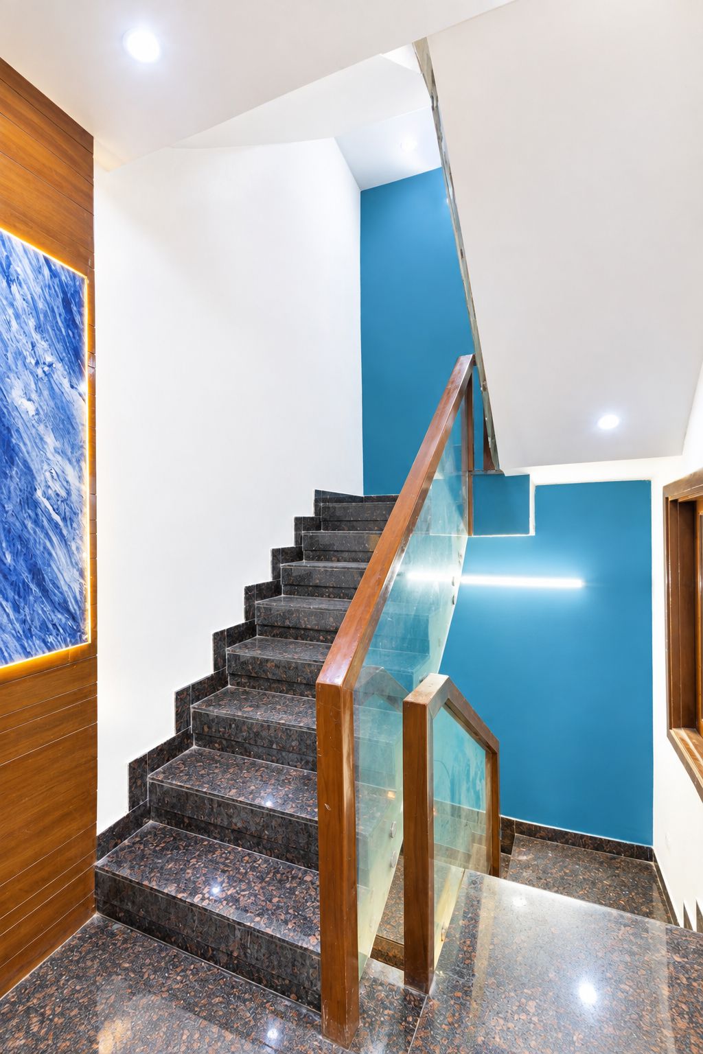 A modern staircase with a glass railing, wooden handrails, and a blue accent wall.