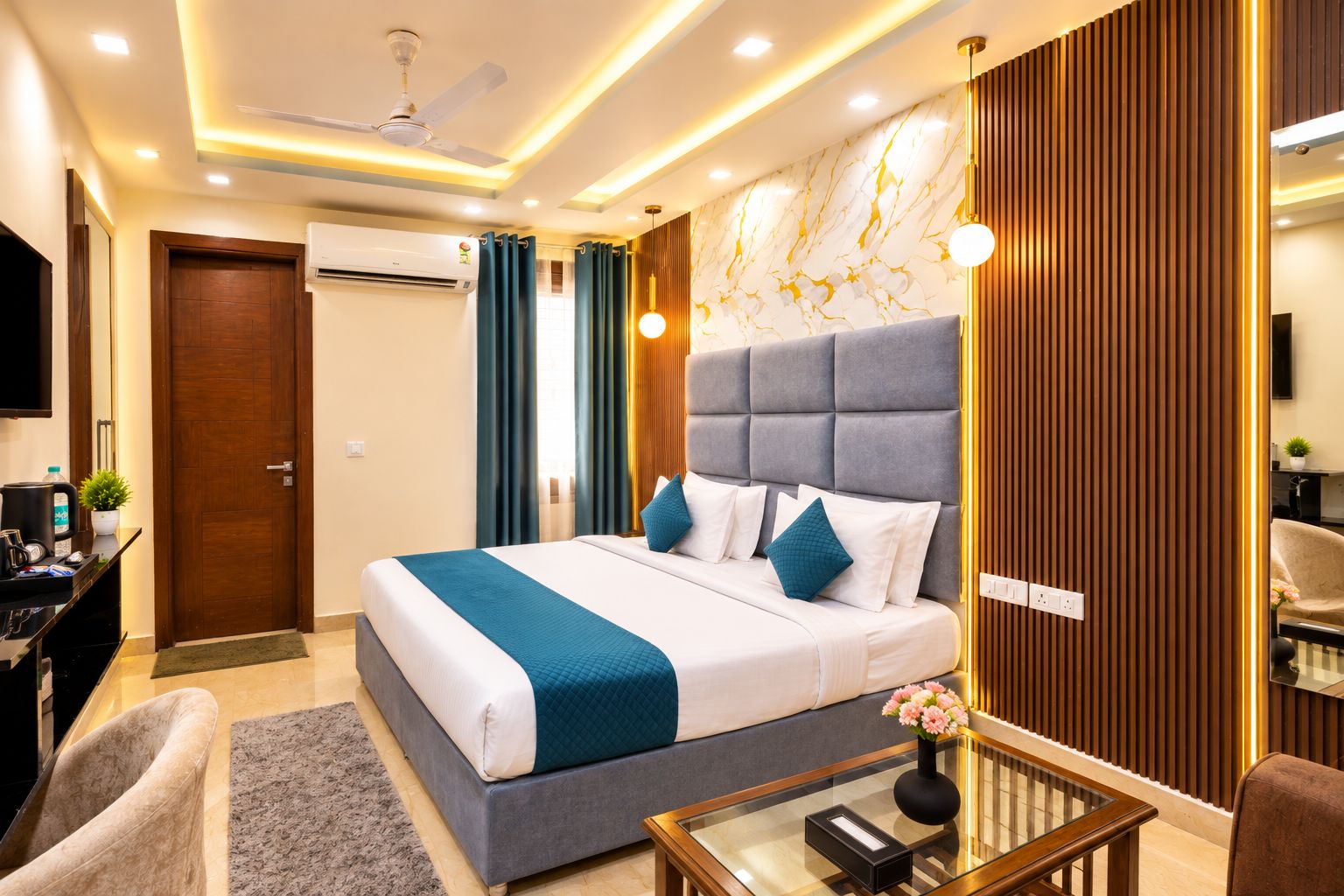 A modern hotel room with a large bed, a desk with a computer, a chair, and a TV.
