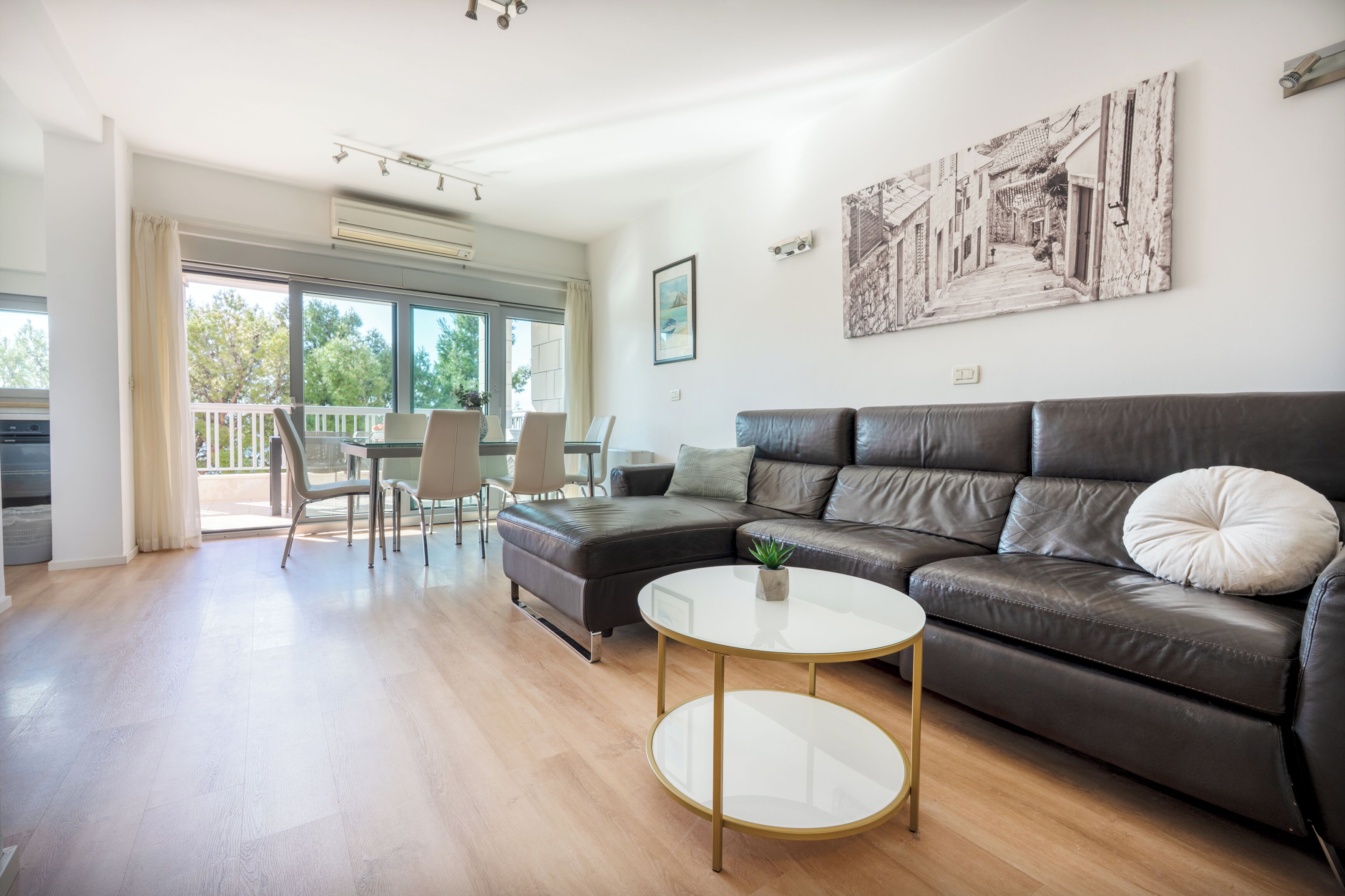 Uma sala de estar moderna com um sofá de couro, uma mesa de centro de vidro e um espaço de jantar com cadeiras e uma mesa.