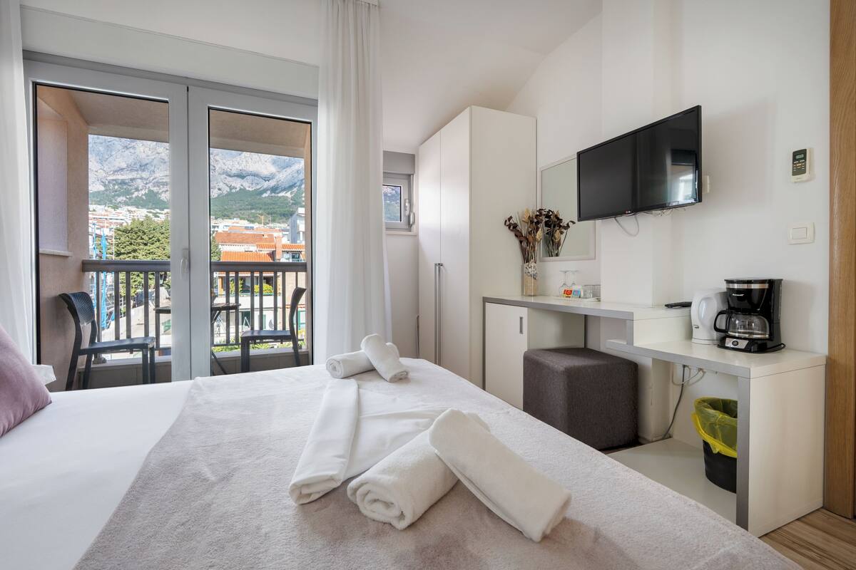 A hotel room with a bed, a desk, a TV, and a balcony with a mountain view.