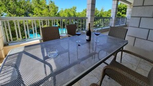 A covered outdoor patio with a metal table and wicker chairs, overlooking a swimming pool and greenery. - Pansion Simic (Makarska)