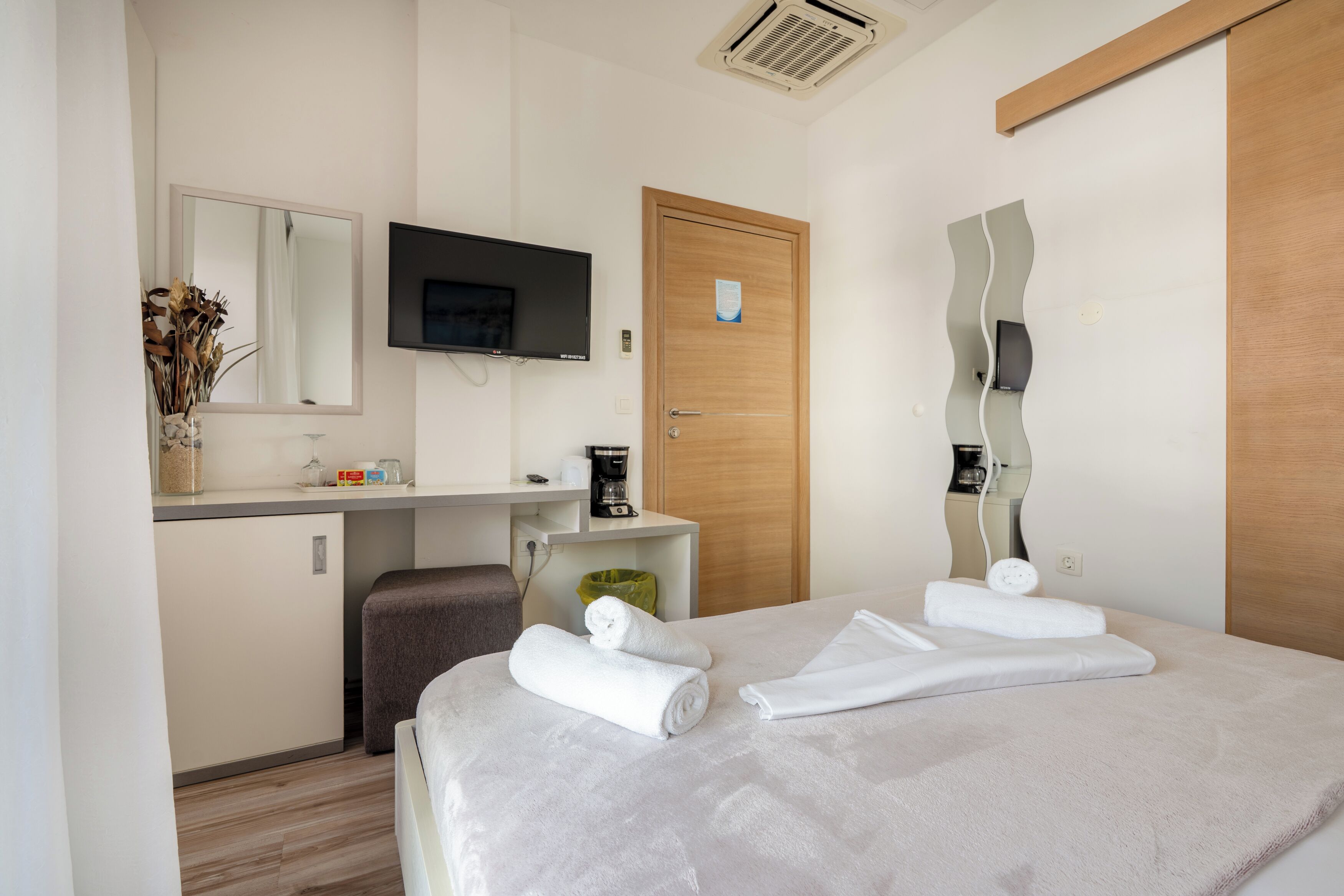 Ein Hotelzimmer mit einem Bett, einem Schreibtisch, einem Fernseher, einer Tür und einem Spiegel.
