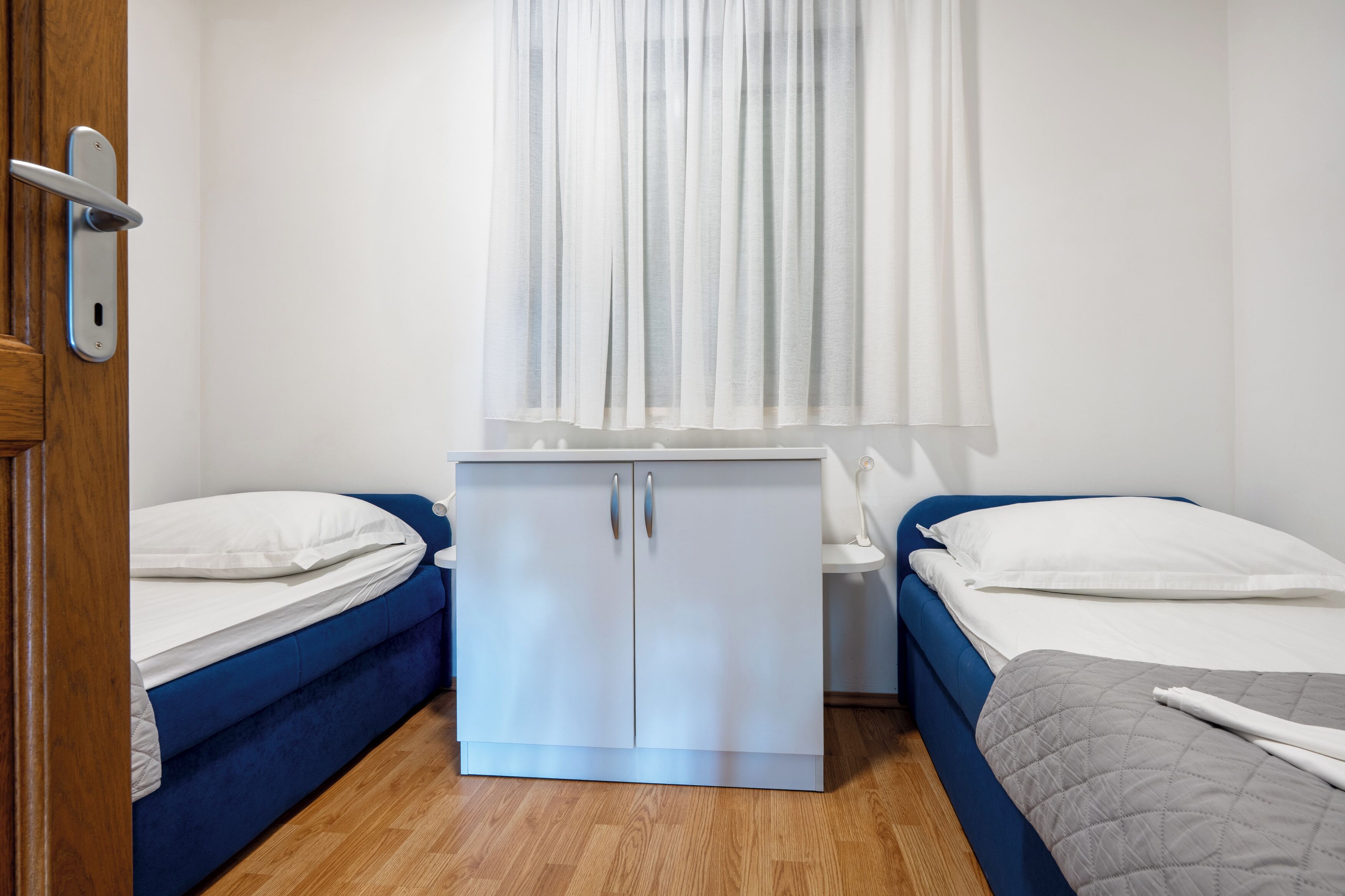 A bedroom with two beds, a wardrobe, and a window with curtains.