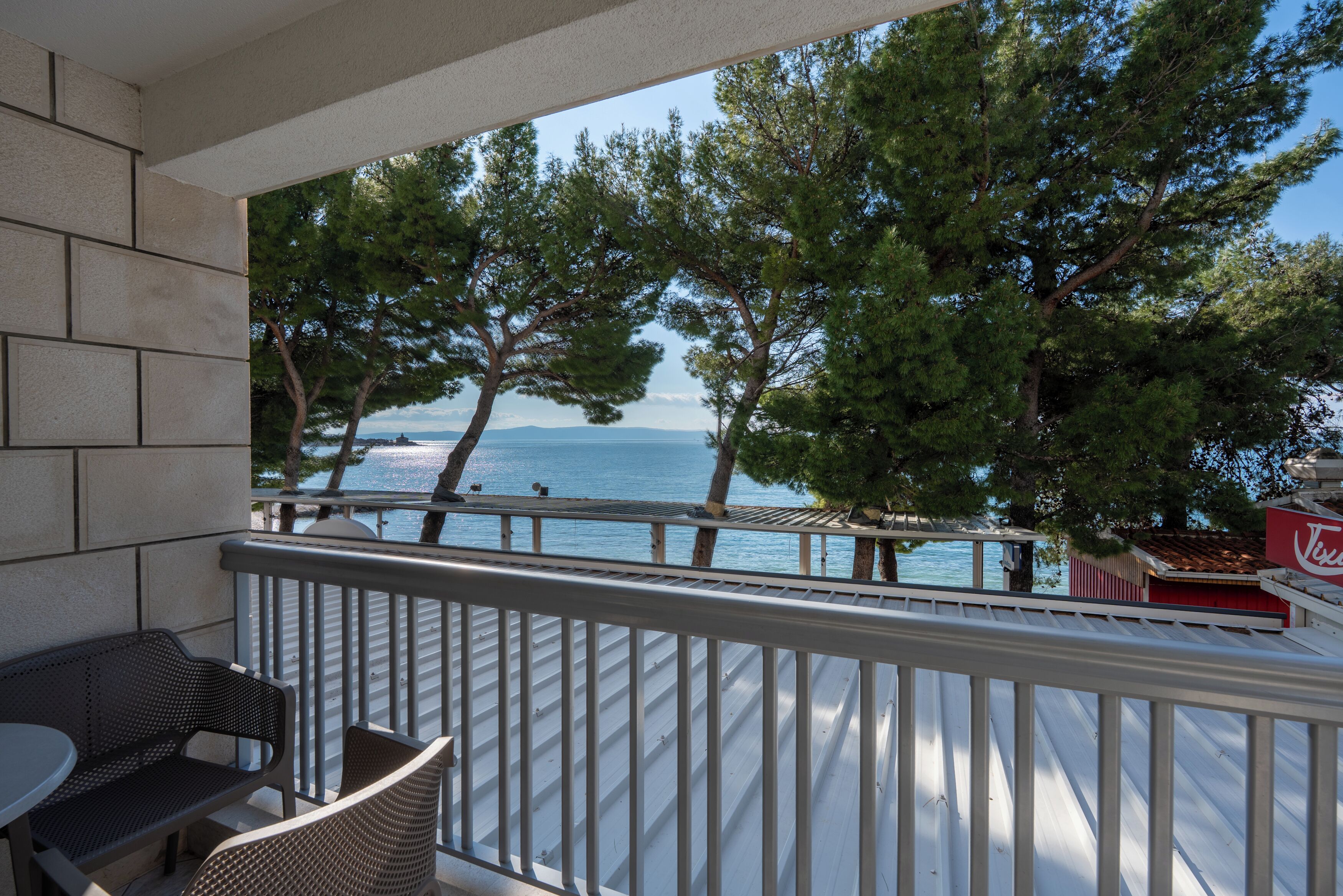 A balcony with a view of the sea and trees, featuring a table and chairs.