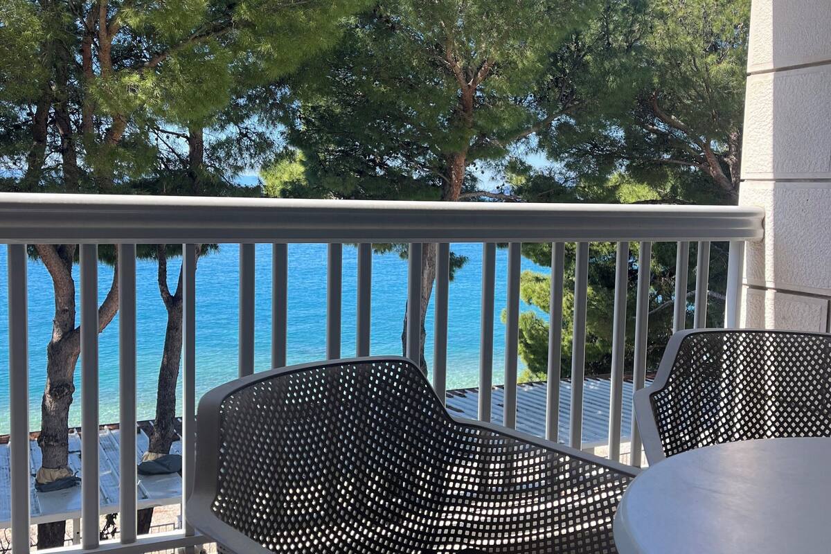 A balcony with a table and two chairs, overlooking a body of water and trees.
