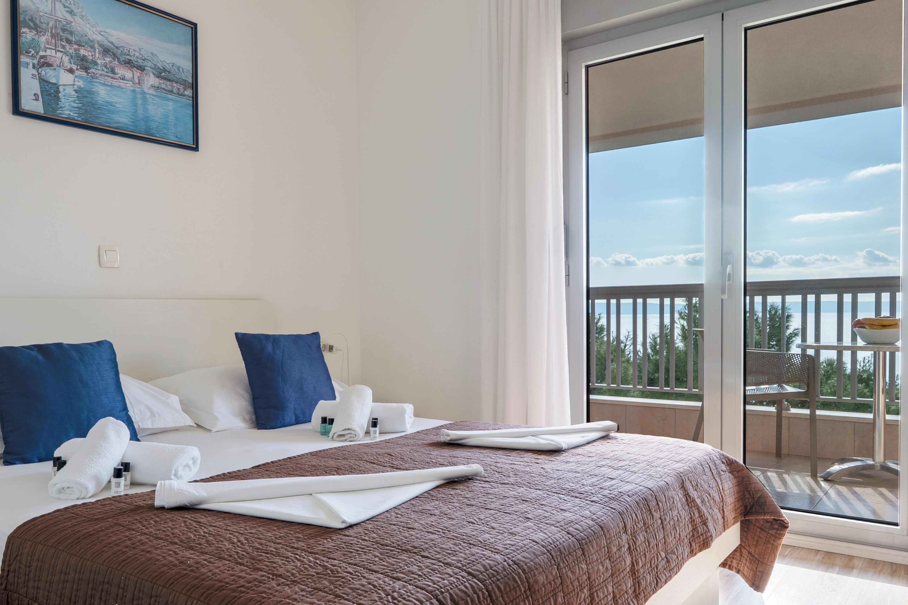 Une chambre d’hôtel avec un lit, des oreillers, des serviettes, un tableau et un balcon avec vue.