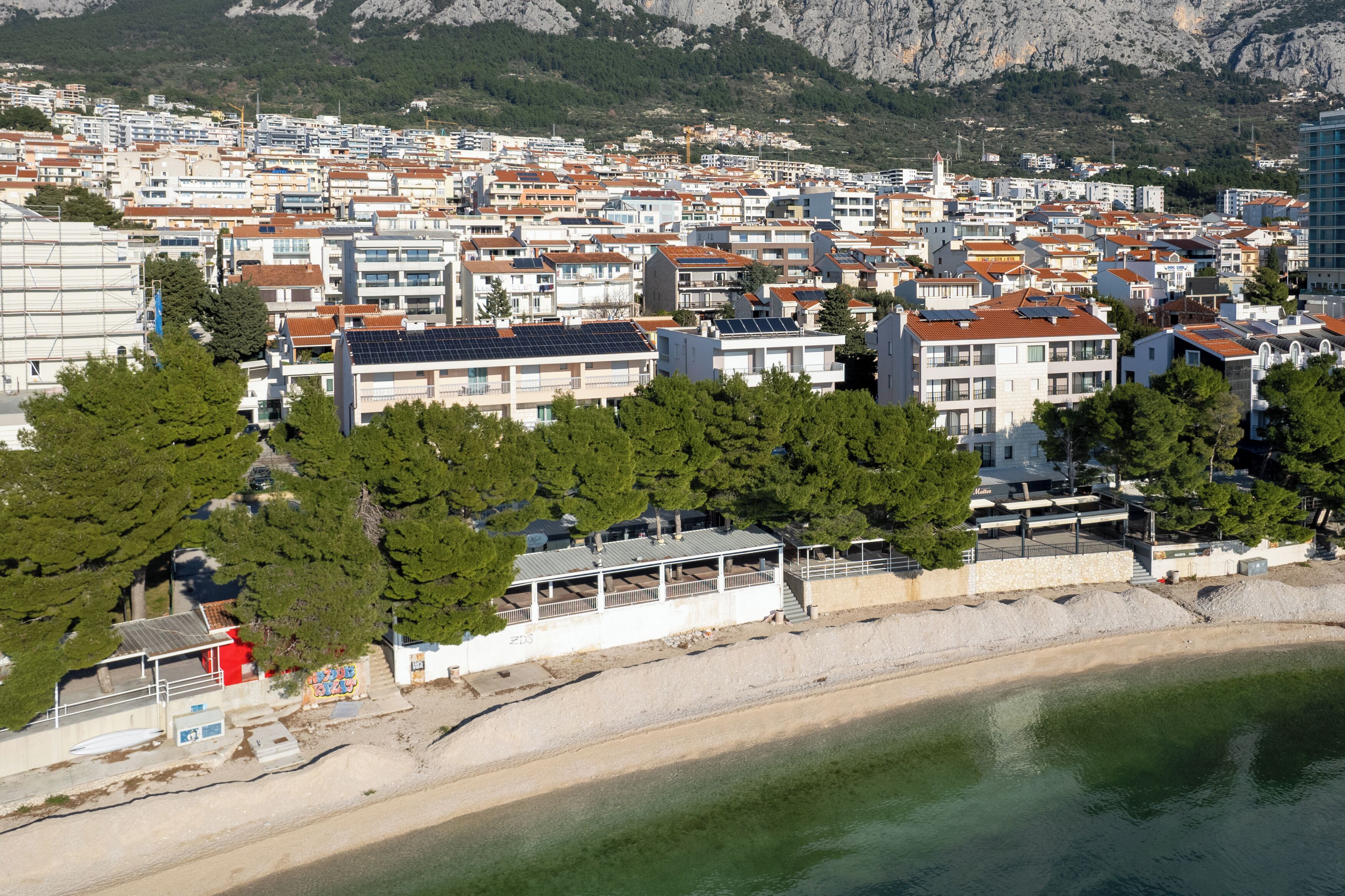 Une ville côtière dotée d’un port de plaisance, de bâtiments aux toits recouverts de tuiles rouges et d’une plage.