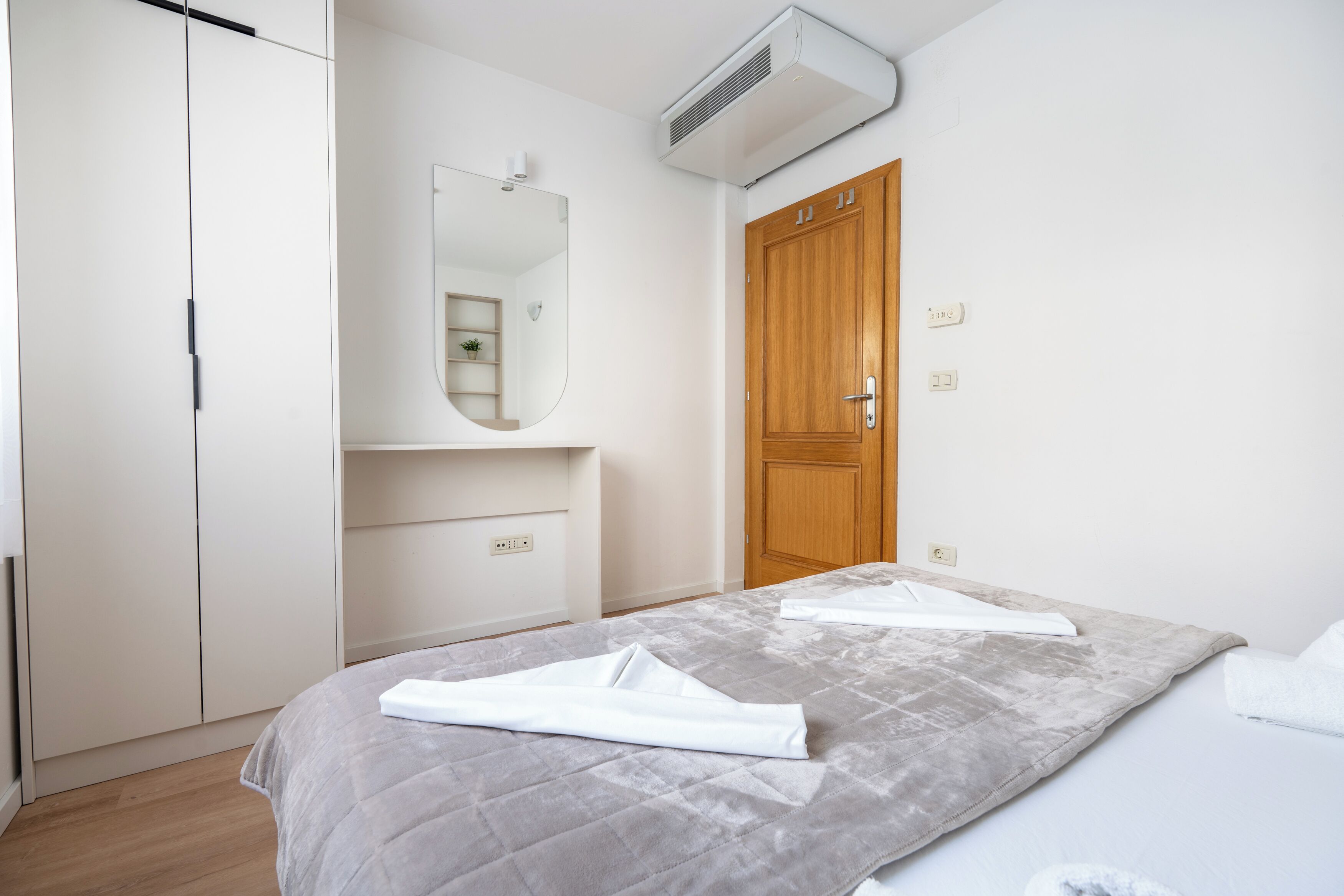 A bedroom with a bed, a wardrobe, a mirror, and an air conditioner.