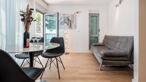 A modern living room with a grey sofa, a glass dining table with four chairs, and a vase with dried plants. - Pansion Simic (Makarska)