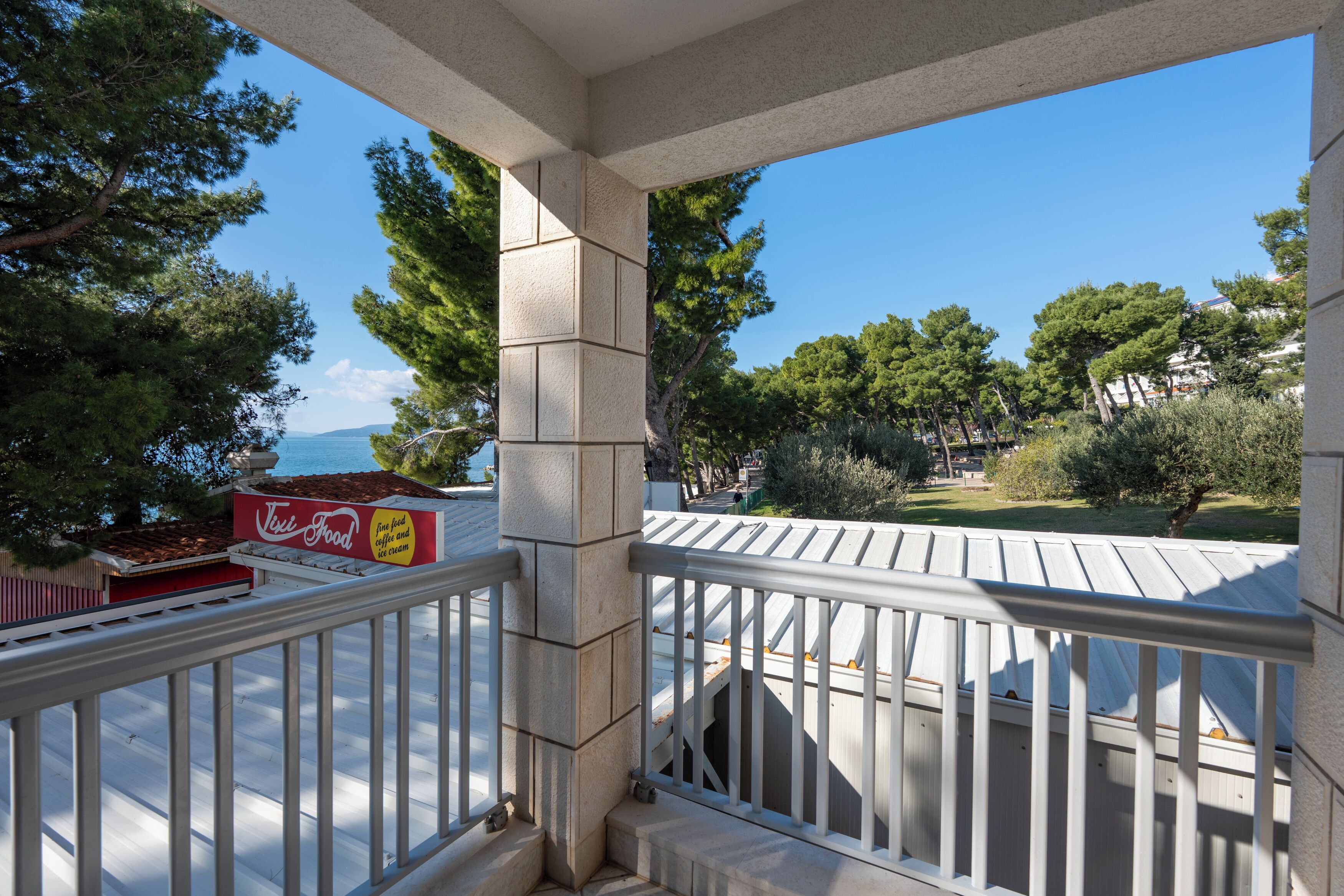 Ein Balkon mit Blick auf eine Küstenlandschaft, ein Schild mit der Aufschrift 'Tiki Food' und eine Steinsäule.
