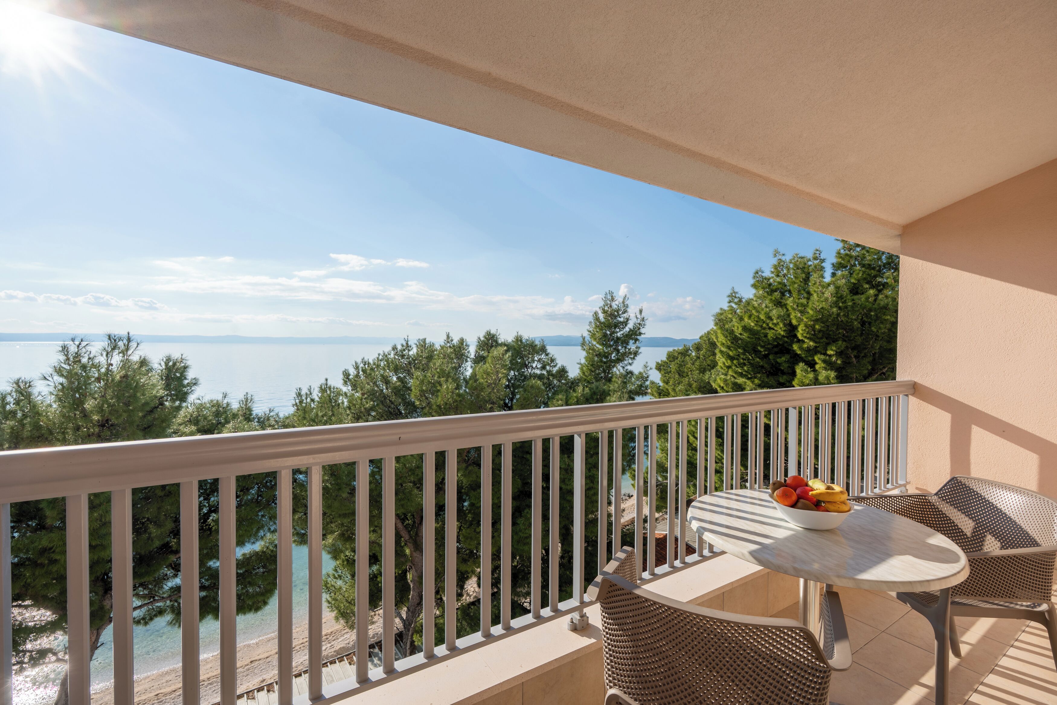 En balkon med et bord og stole, med udsigt over en strand og havet.