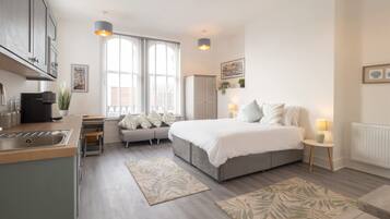 A modern bedroom with a large bed, bedside tables, a sofa, and a kitchen area with a sink and cabinets.