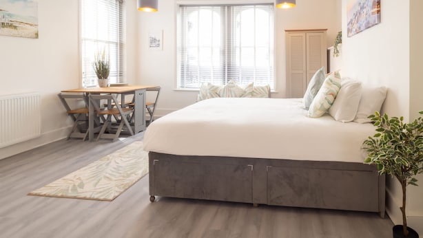 A bedroom with a large bed, a desk with chairs, and a window with blinds. - Host Stay Harbour Lights (Ramsgate)