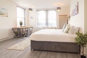Une chambre avec un grand lit, un bureau avec des chaises et une fenêtre avec des stores.