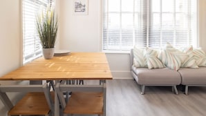 A dining area with a wooden table and benches, a potted plant, a sofa with striped cushions, and a window with blinds. - Host Stay Harbour Lights (Ramsgate)