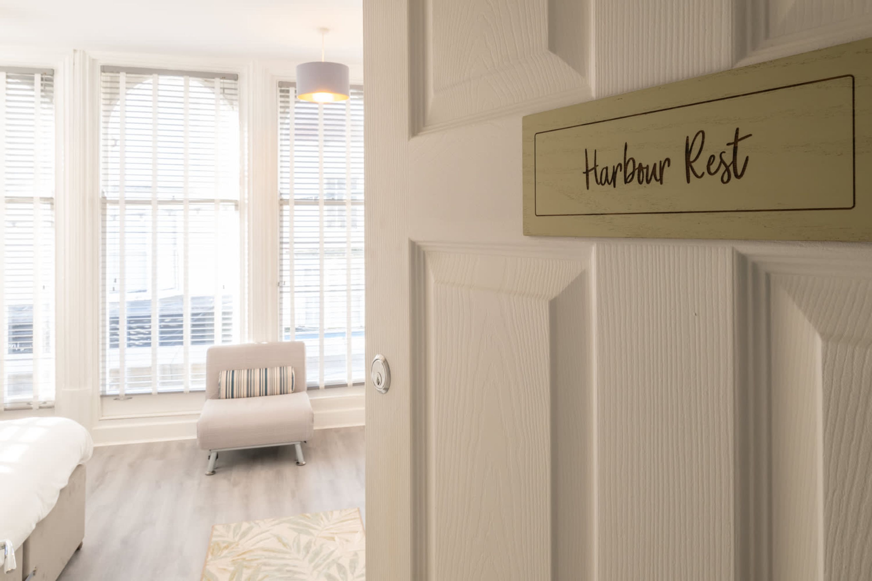 Et hotelværelse med en seng, en sofa, et vindue med rullegardiner, og et skilt med teksten "Harbour Rest".