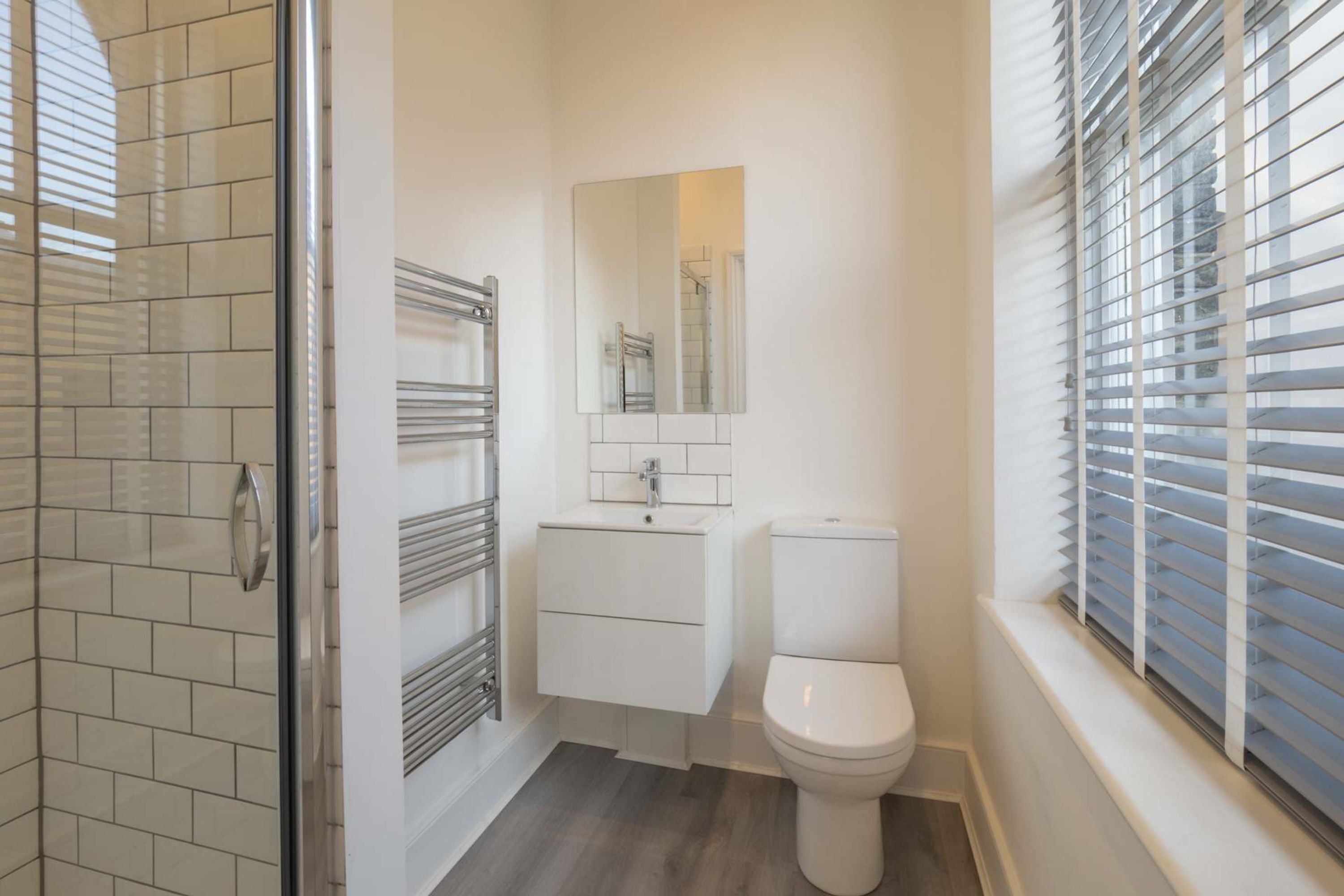 A bathroom with a glass shower enclosure, a white sink with a mirror above it, and a toilet.