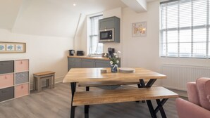 A modern kitchen with a wooden table and bench, a microwave, and a coffee maker. - Host Stay The Crow s Nest (Ramsgate)