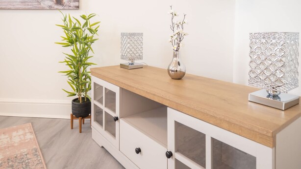 A white wooden console with glass doors, a potted plant, and two crystal lamps. - Host Stay The Crow s Nest (Ramsgate)