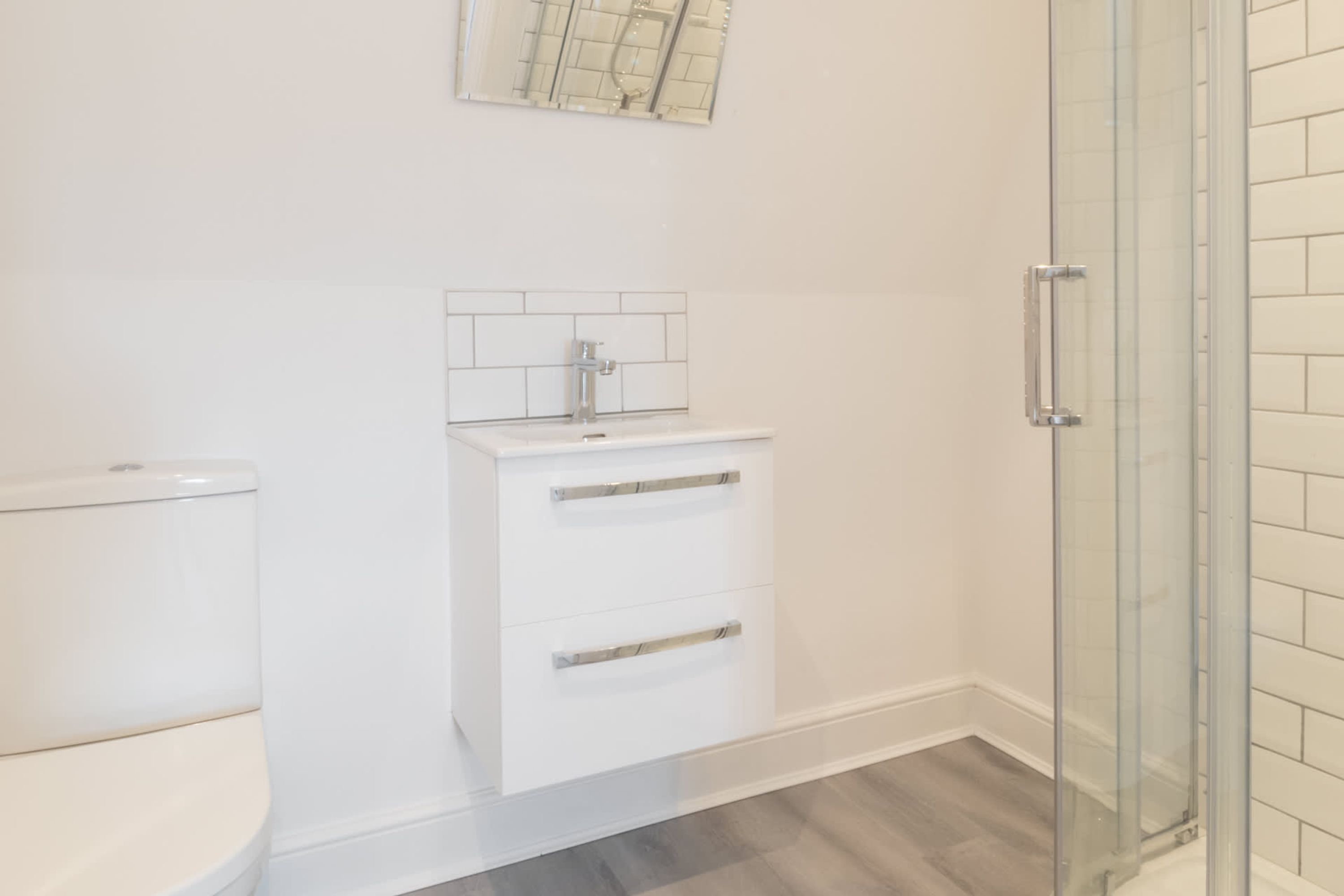 Een badkamer met toilet, een witte wastafel met spiegel erboven en een douchecabine met glazen wanden.