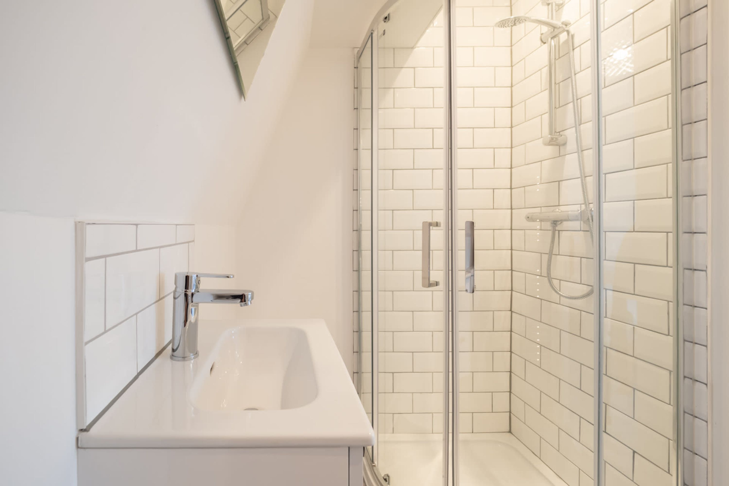 A modern bathroom with a glass-enclosed shower, white tiles, and a white sink.