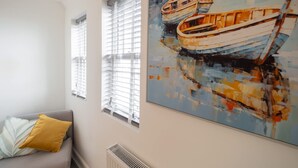 A room with a gray sofa, a yellow pillow, and a large painting of boats on the wall. - Host Stay The Crow s Nest (Ramsgate)