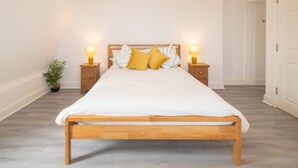 A neatly made bed with a wooden frame and white bedding, flanked by two bedside tables with lamps, in a room with a simple, clean design. - Host Stay The Crow s Nest (Ramsgate)