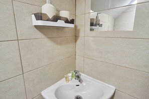 Une salle de bain avec un lavabo blanc, un miroir et une étagère contenant des articles de toilette.