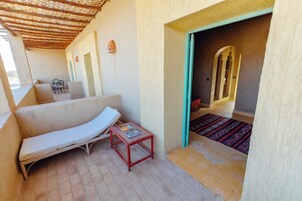 Una habitación con un sofá blanco, una mesita con libros, una alfombra estampada y un vano que da a otra estancia.