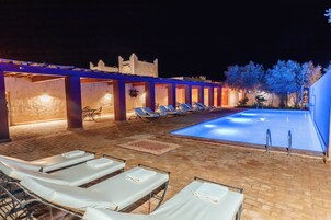 Zona junto a la piscina con sillones de descanso y una piscina por la noche.