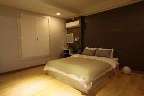 A bedroom with a bed, a bedside table, a mirror, an air conditioning unit, and a window with blinds.